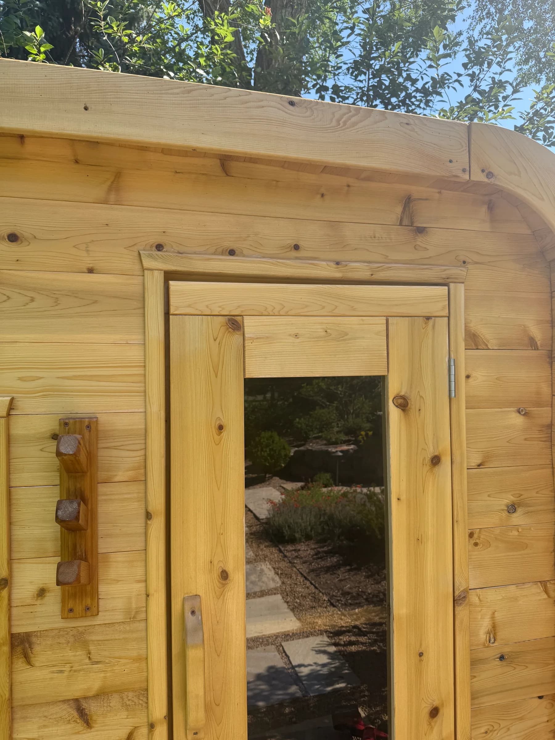 A cedar door and frame on a finished outdoor cabin, a garden path reflected in the glass.